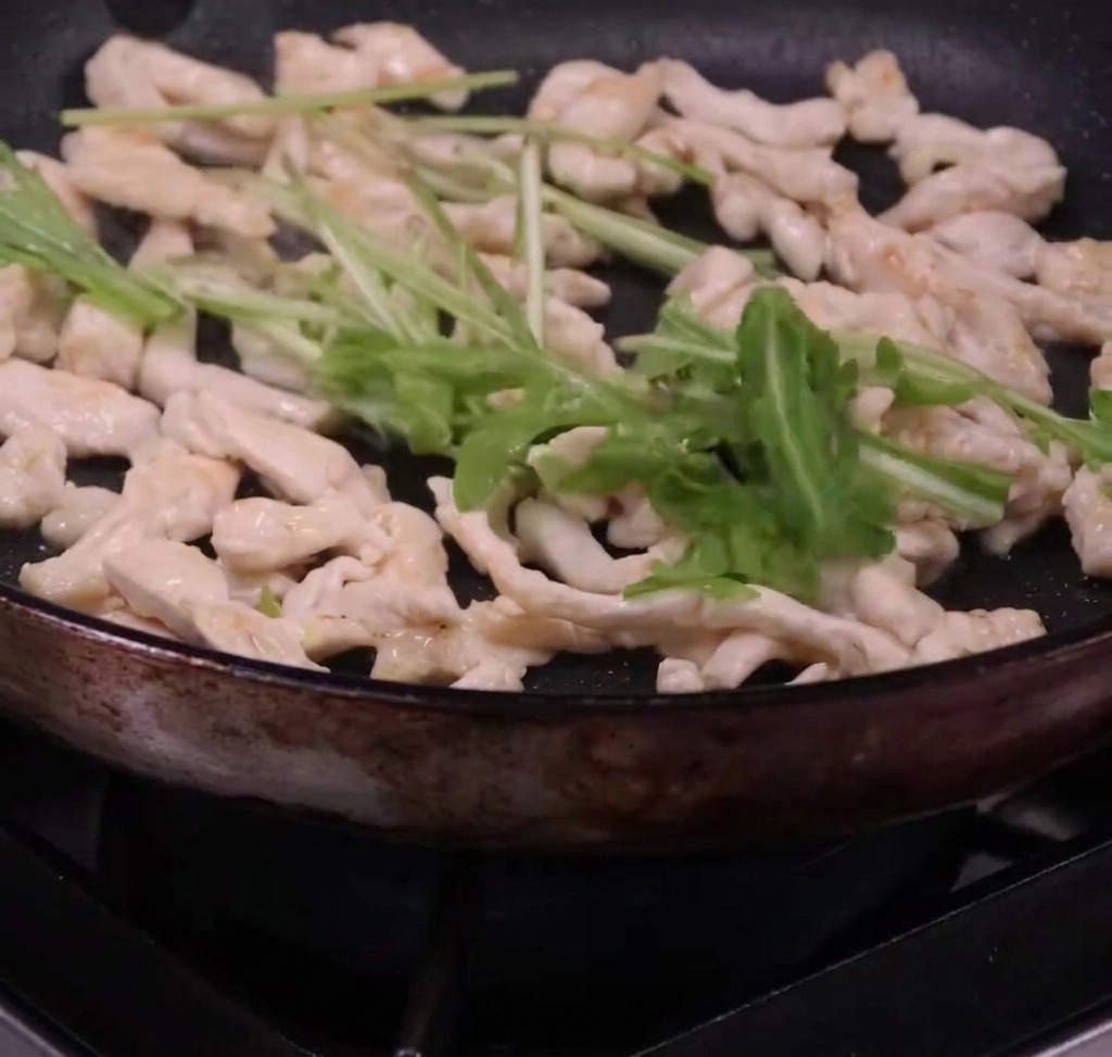 フライパンでパスタとルッコラ、鶏肉を一緒に和えている様子。