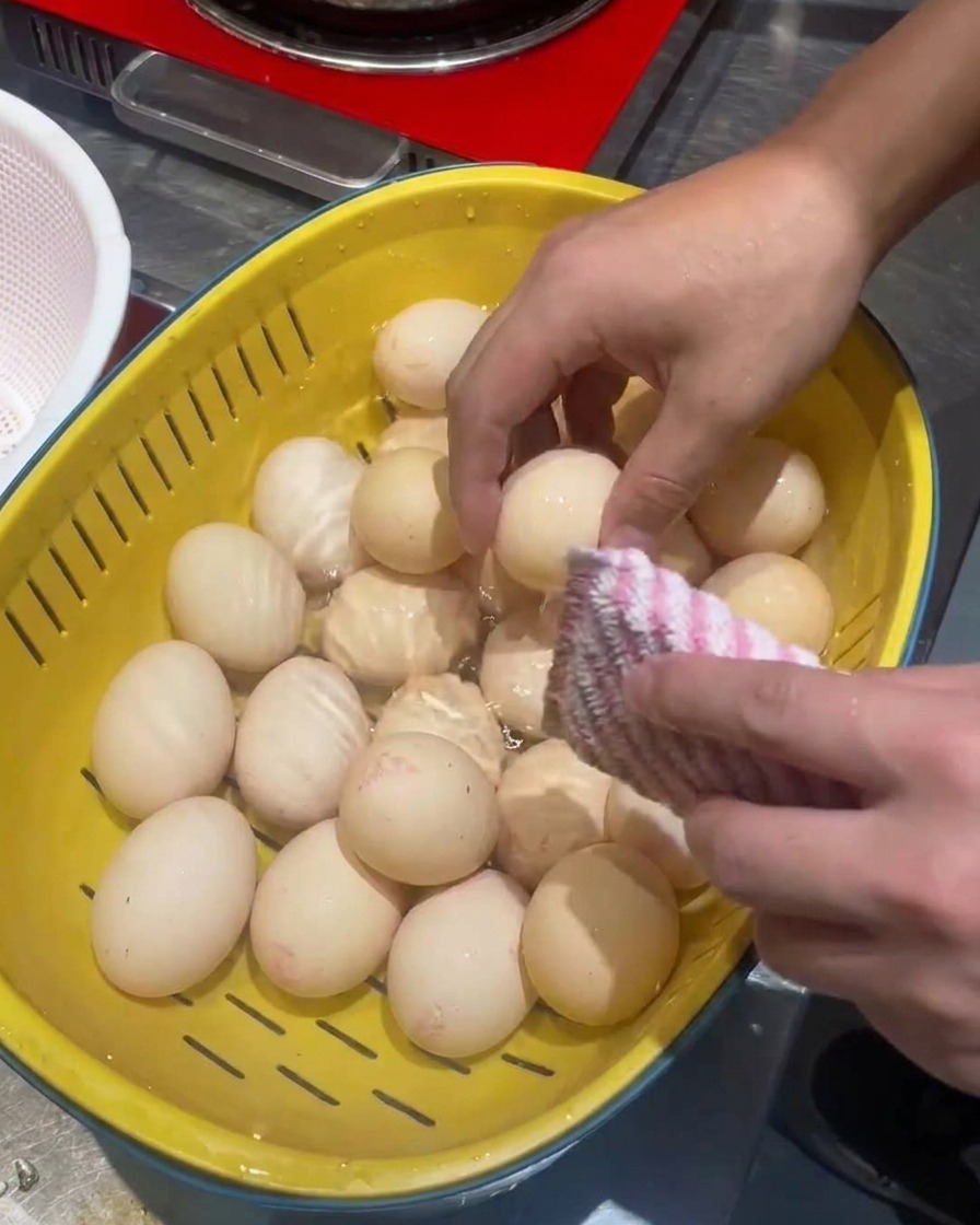 黄色いザルに入った卵をたわしで丁寧に洗っている様子。