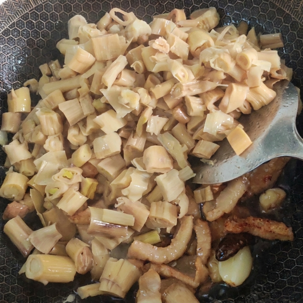 具材が入った鍋に水と高菜を加えて煮込んでいる様子。