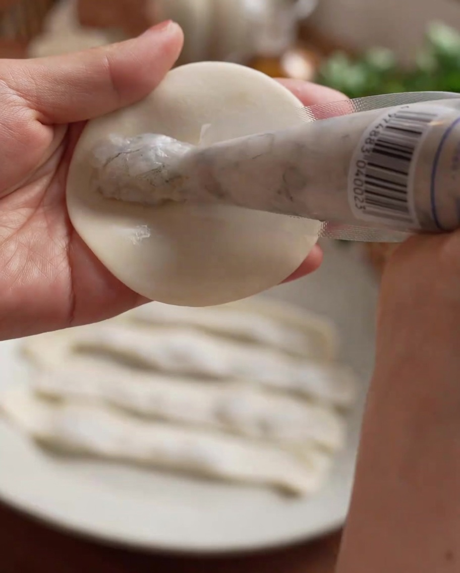 絞り袋を使って、餃子の皮の中央にまっすぐ海老ペーストを絞り出している様子。