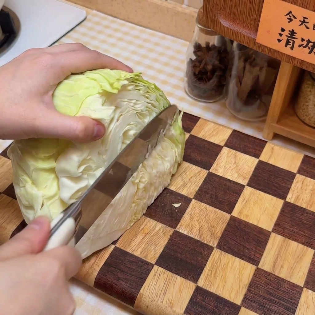 チェック柄の木製まな板の上でキャベツを千切りにしている様子。
