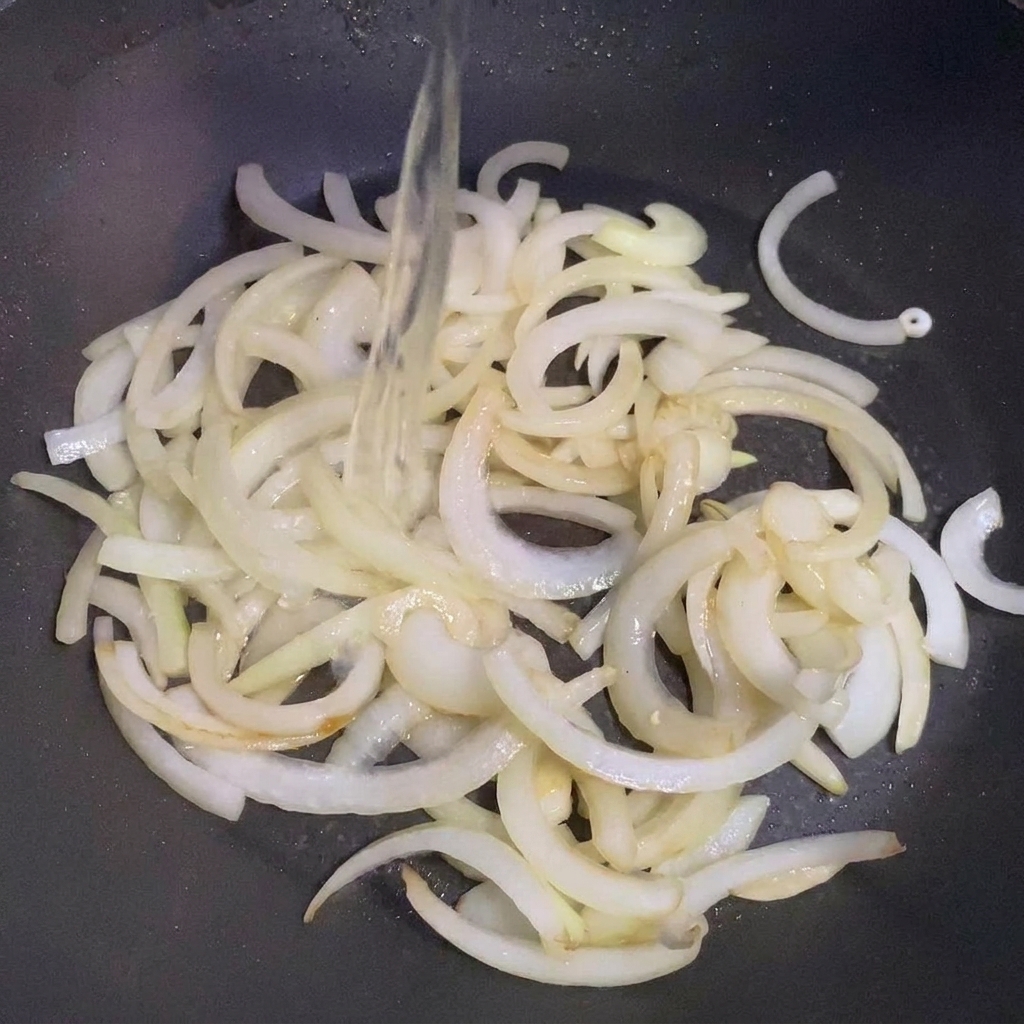 炒めた玉ねぎの入ったフライパンに酒を注いでいる様子