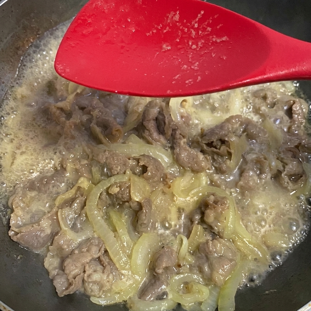 煮込んでいる牛肉と玉ねぎに薄口醤油を加えている様子