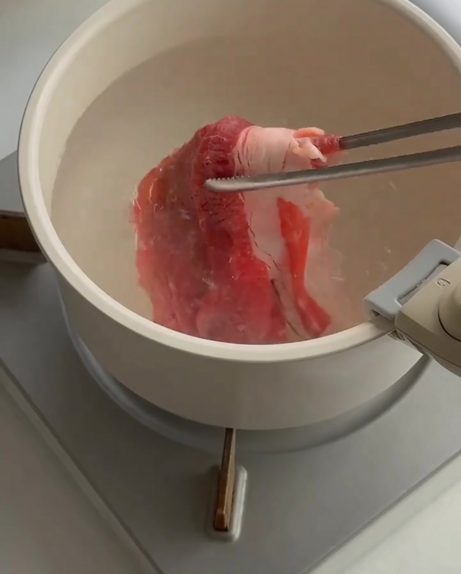 トングで熱湯の鍋に薄切りの生牛肉を入れている様子。