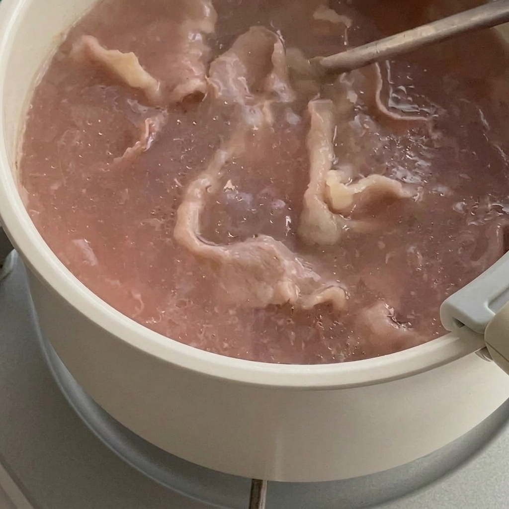鍋の中で色が変わり始めた牛肉を、網杓子ですくい上げている様子。