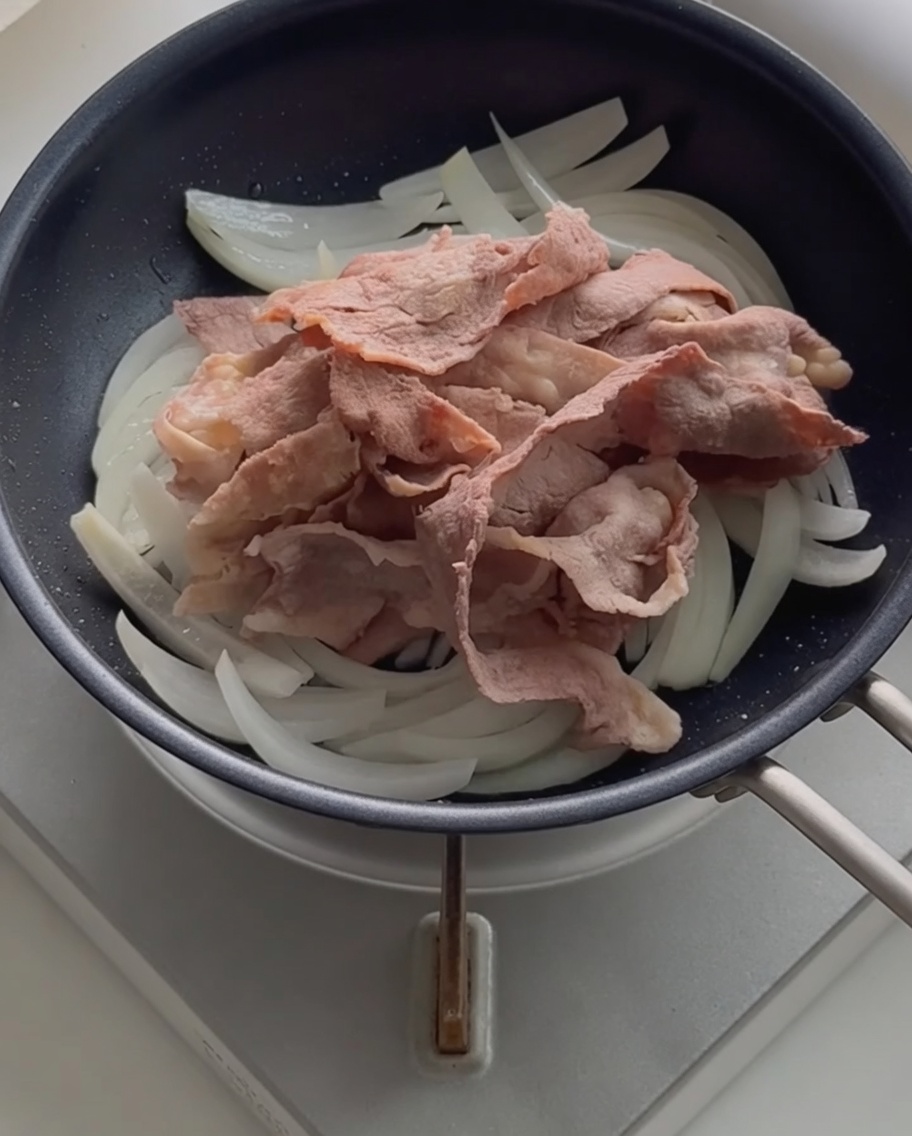 炒めた玉ねぎの上に下ゆでした牛肉を重ねている様子。
