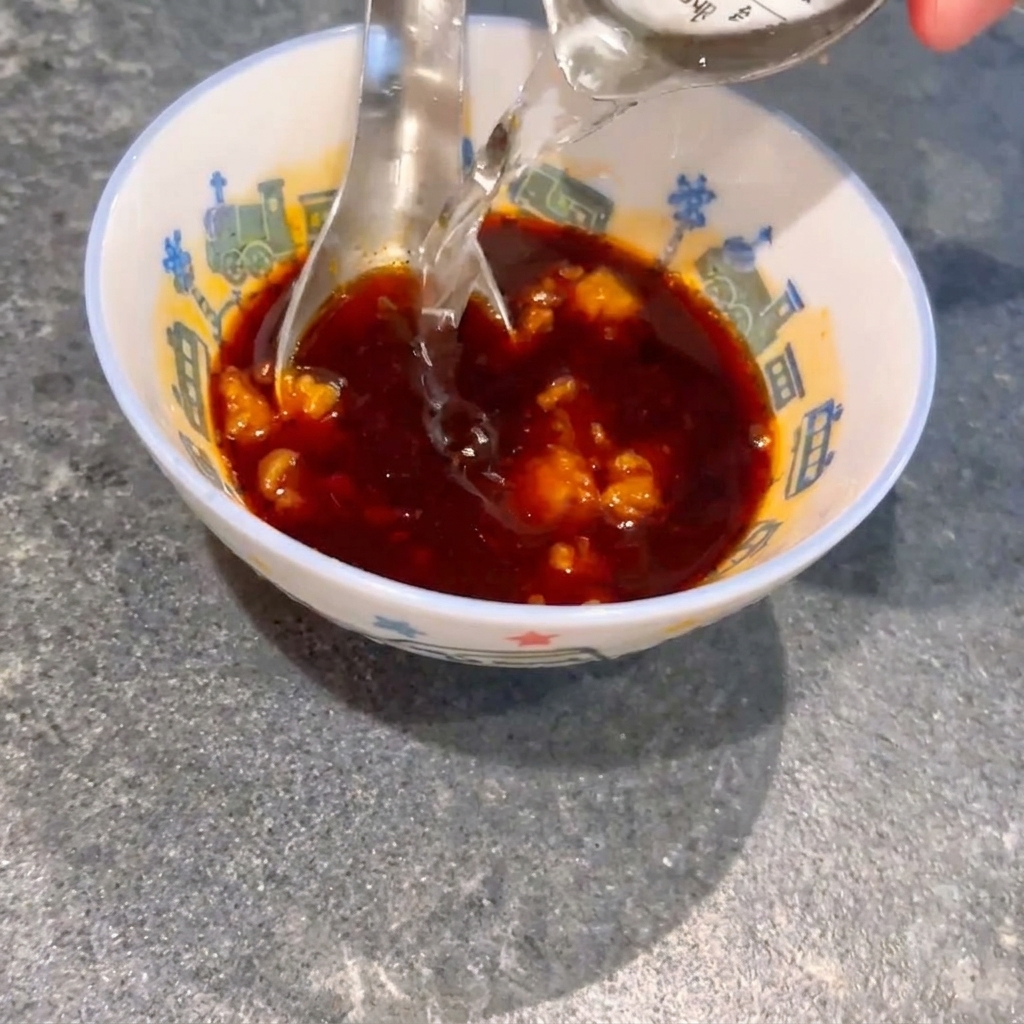 醤油と味噌の入ったボウルに水を加え、スプーンで混ぜている様子。