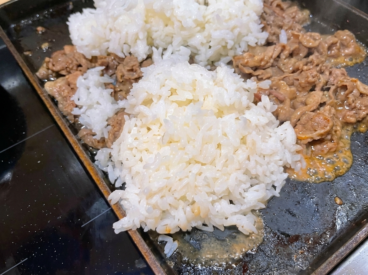 炒めた牛肉の上に炊いたご飯を投入する様子。
