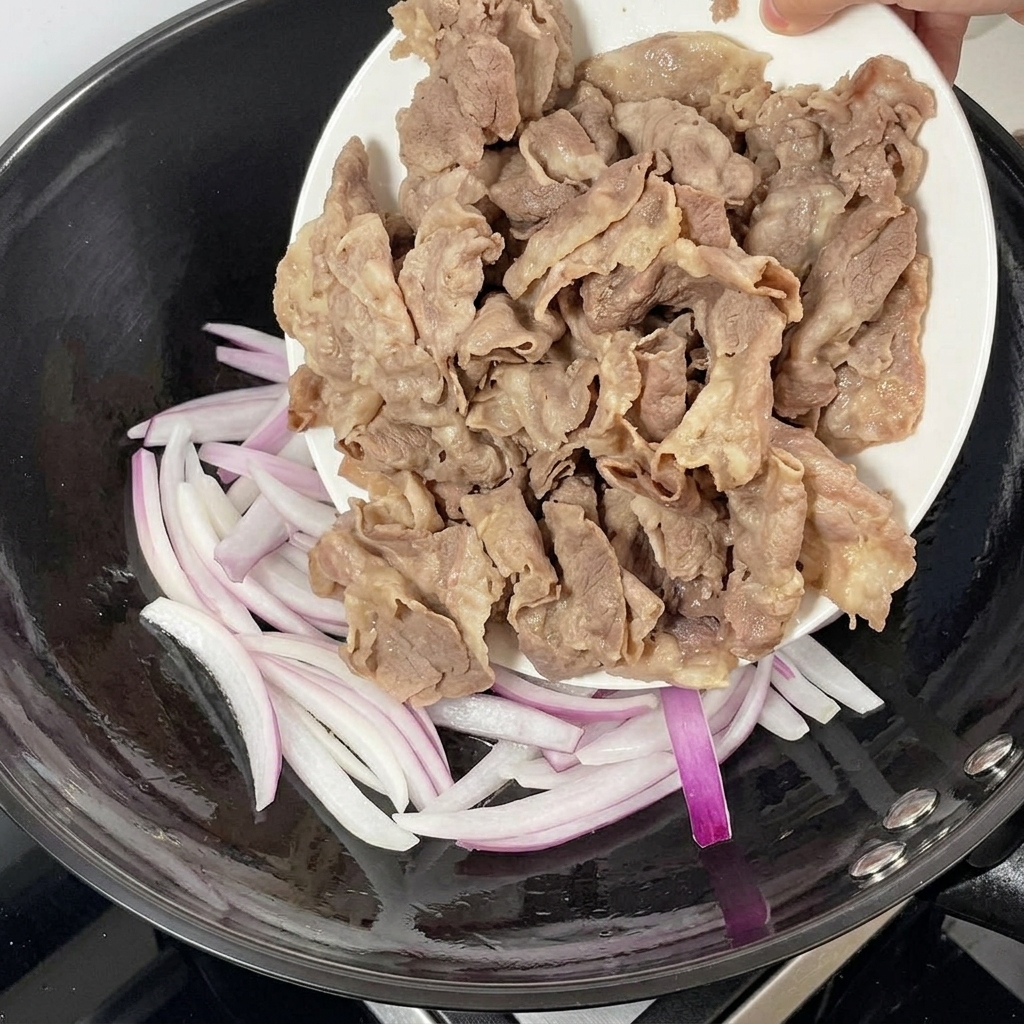 炒めた赤玉ねぎのフライパンに湯通しした牛肉を加える様子。