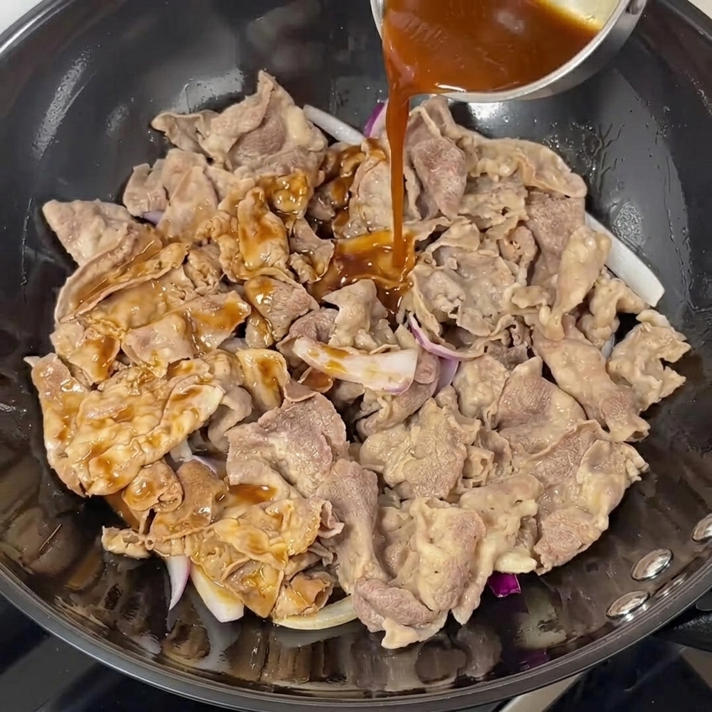 牛肉と玉ねぎの上から濃い照り焼きダレをかける様子。