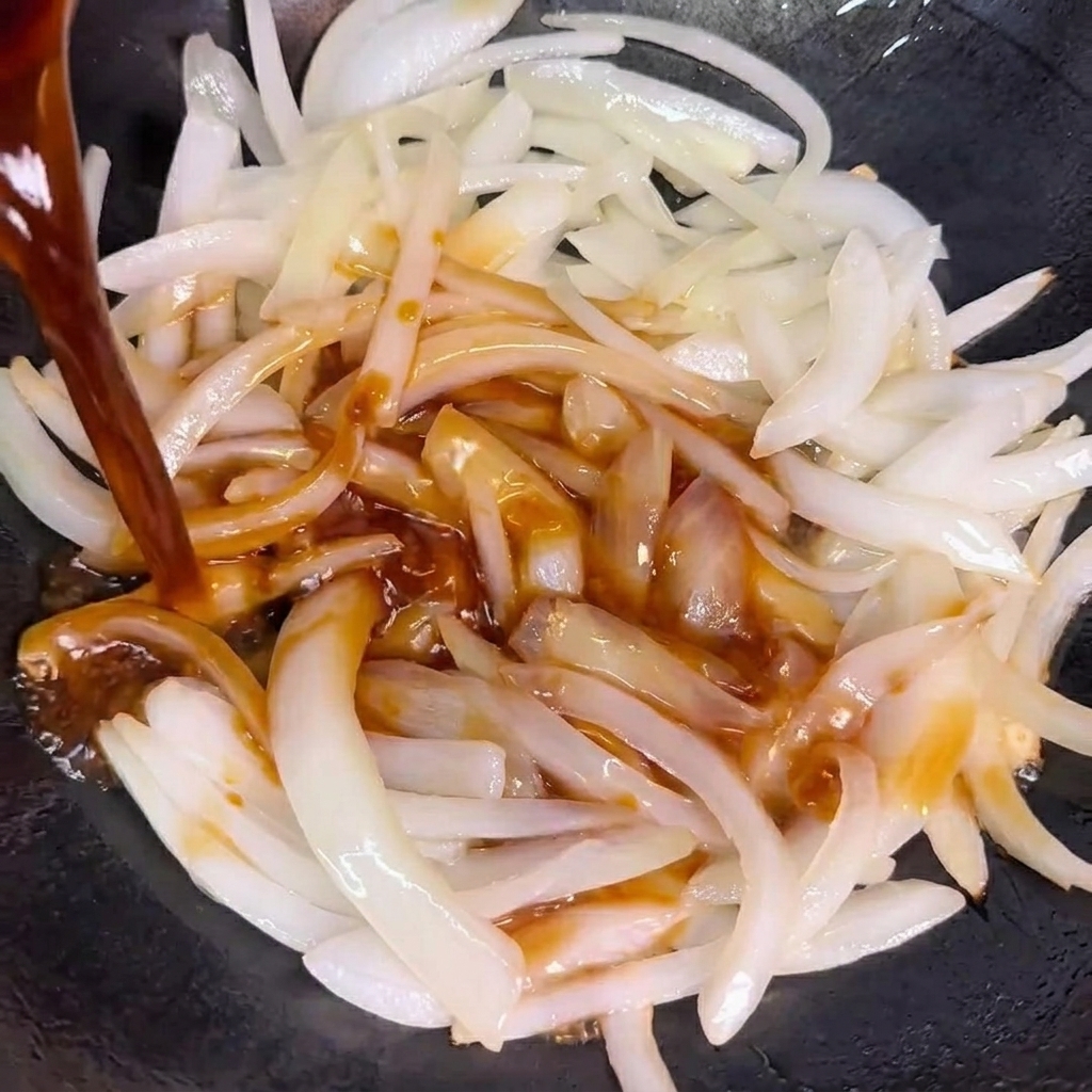 炒めた玉ねぎにタレを注ぎ入れる様子。
