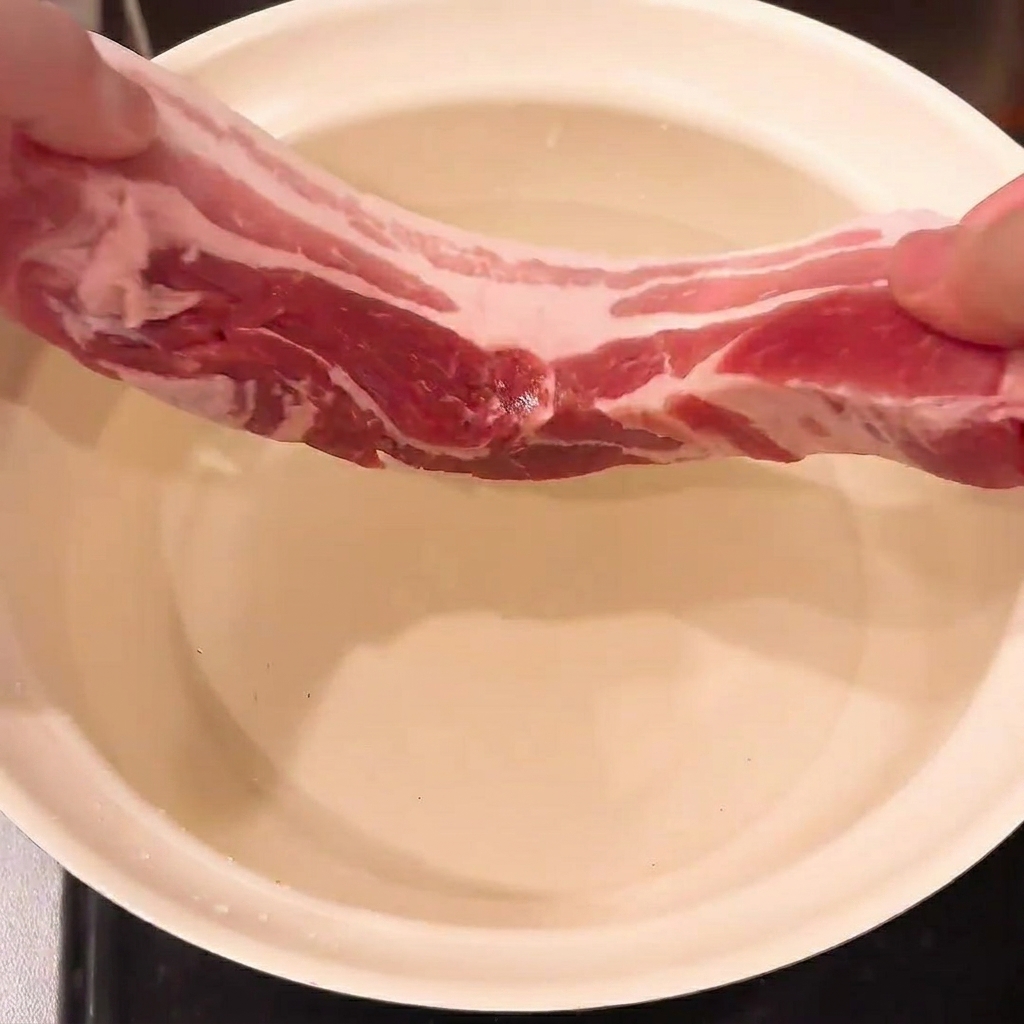 鍋の中で水、長ネギ、生姜とともに下茹でされる豚バラ肉