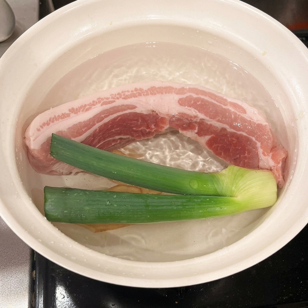 豚肉とネギ、生姜が入った鍋に酒を注ぐ様子