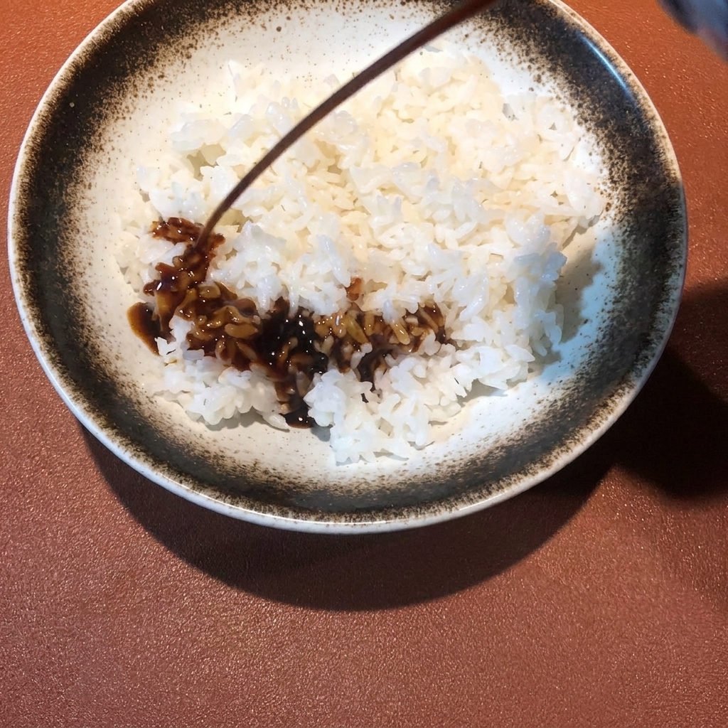 炊きたてのご飯の上に、濃い色のタレを回しかけている様子。