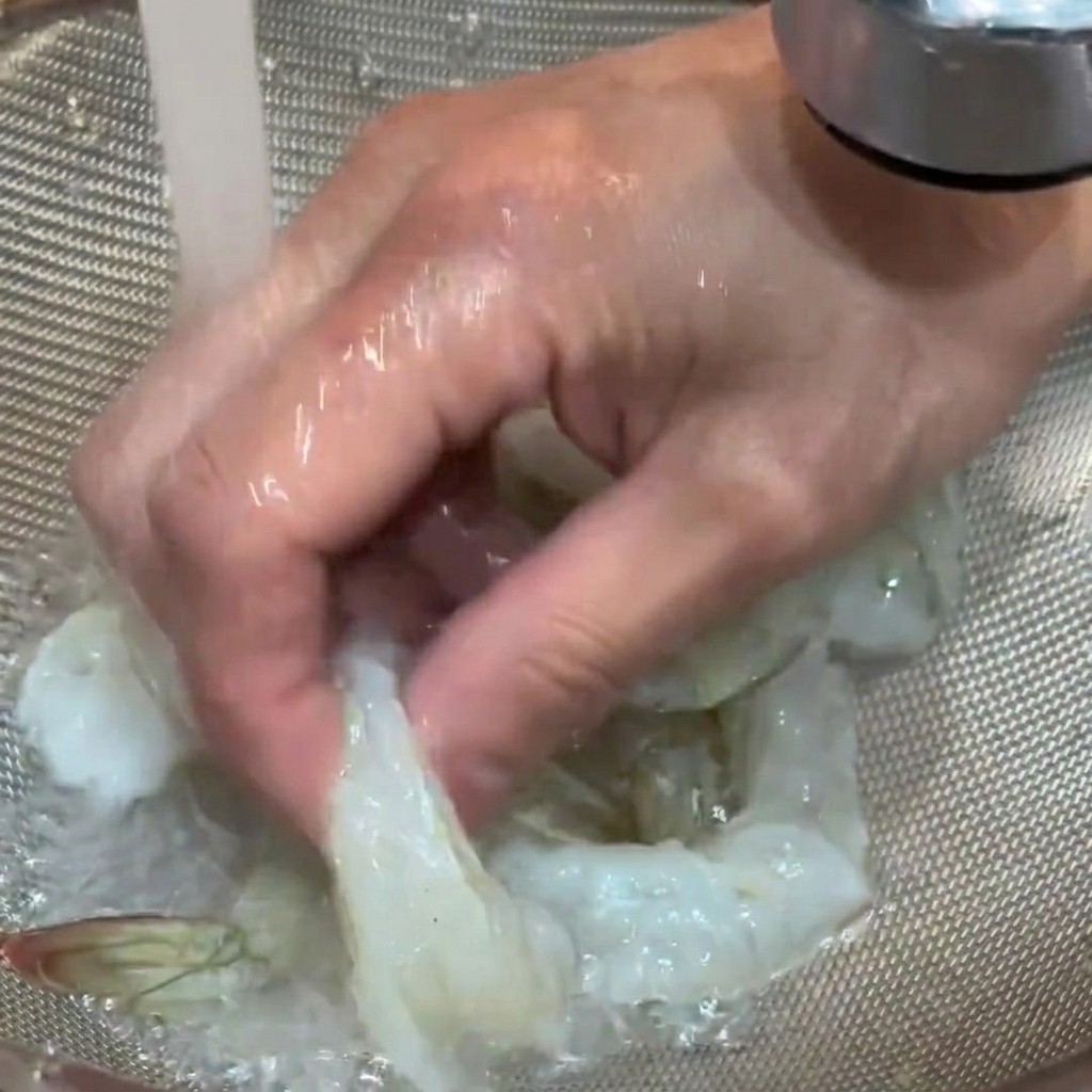 ザルに入れた生海老を流水で洗っている様子。