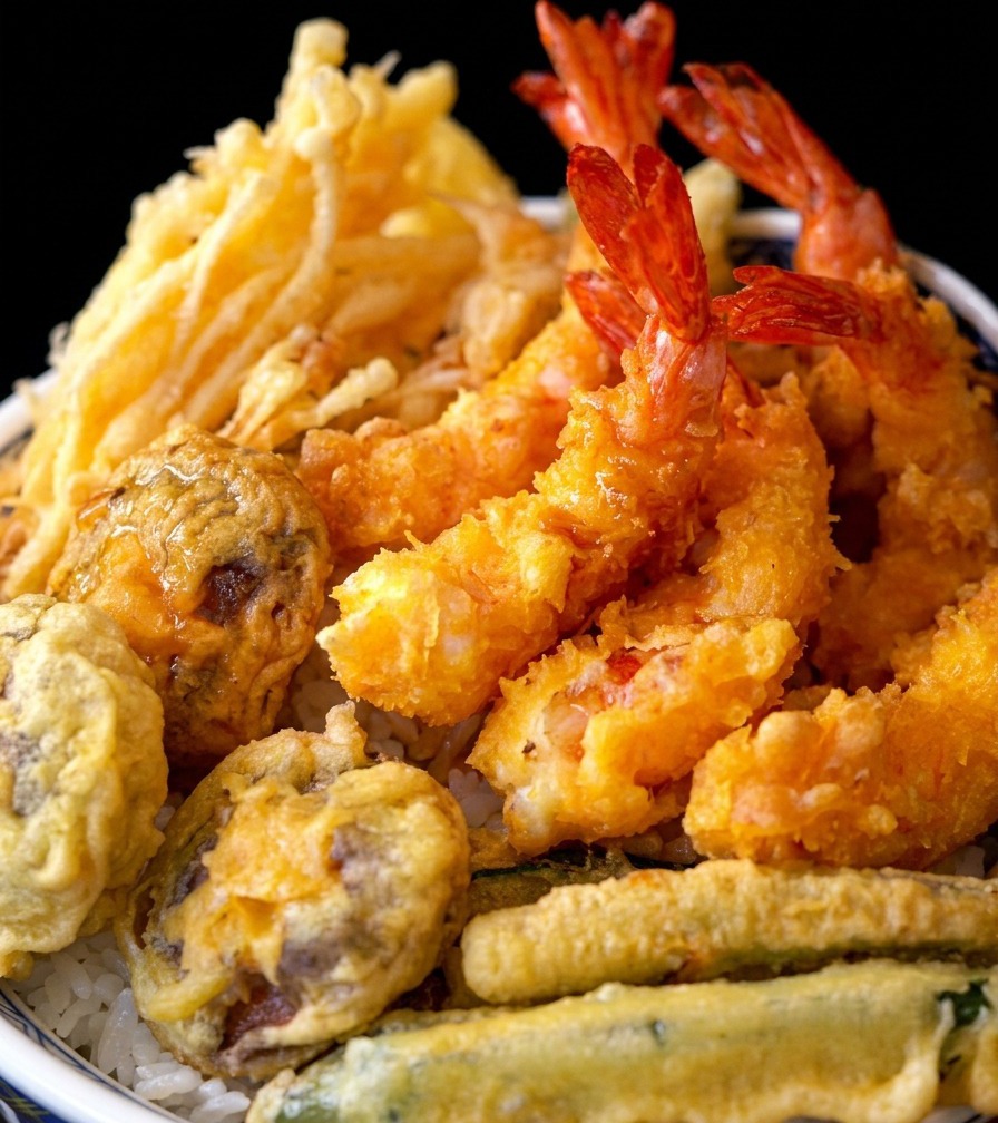丼のご飯の上に、揚げたての天ぷらがきれいに並べられている様子。