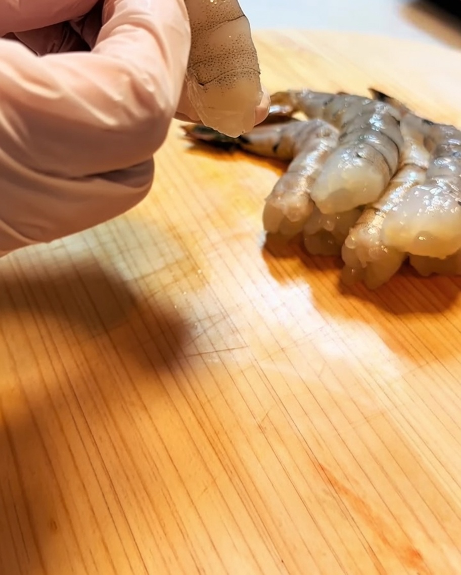 ピンク色の手袋をして、背わたを取り除いた海老をまな板の上で整えている様子。