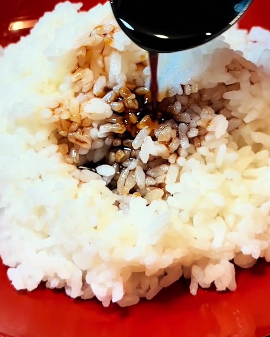 温かいご飯にタレをかけ、天ぷらを盛り付けている様子。