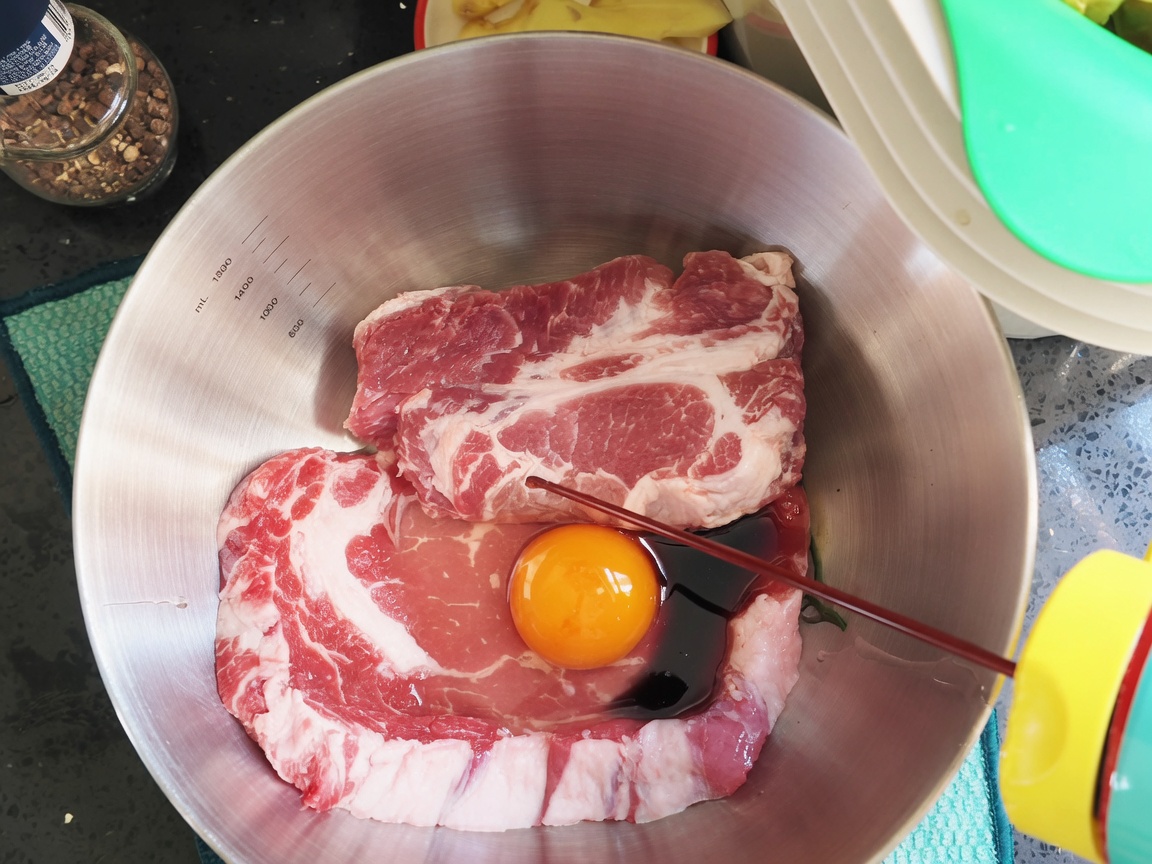 ボウルの中の肉と卵に、醤油や調味料を加えていく様子。