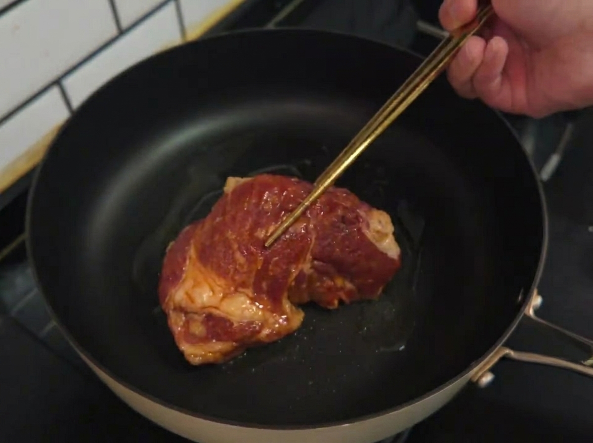 熱したフライパンに油をひき、下味をつけたポークチョップを並べている様子。