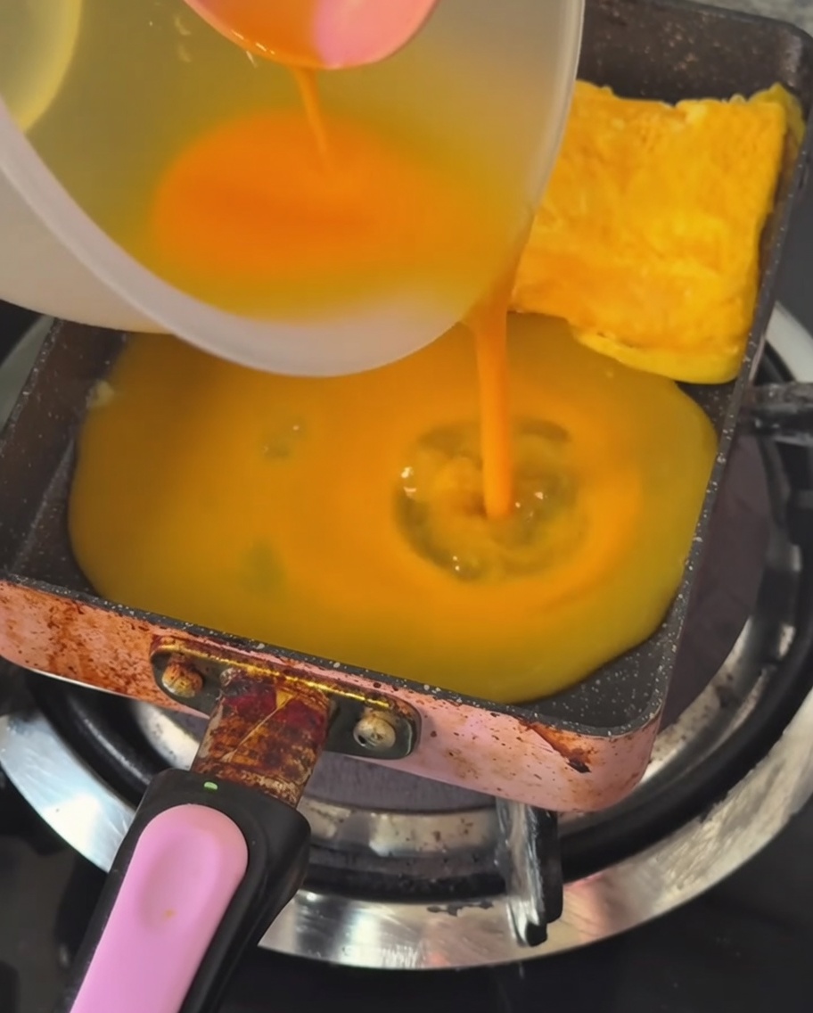 玉子焼き器に薄く卵液を流し込んでいる様子。