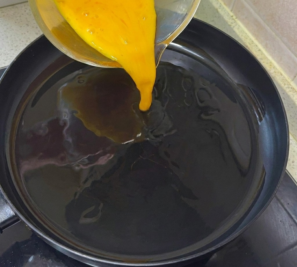 油を引いたフライパンに卵液を流し入れる様子。