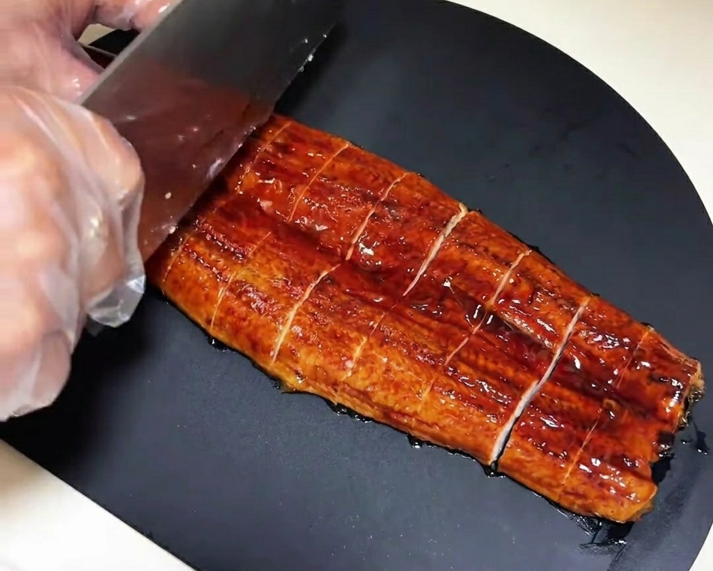 まな板の上で鰻の蒲焼きを一口サイズに切り分けている様子。