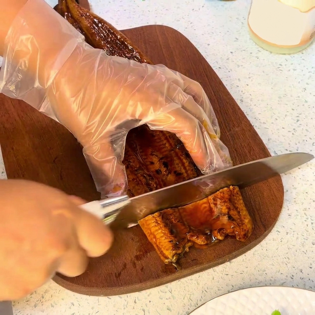 まな板の上でうなぎの蒲焼を包丁で切っている様子。