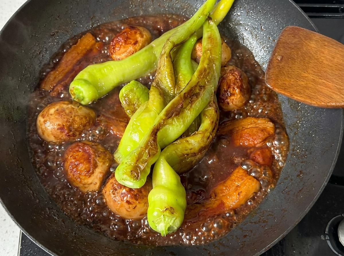 濃厚な色の煮汁の中で、豚バラ肉やゆで卵と一緒に煮込まれているピーマン。