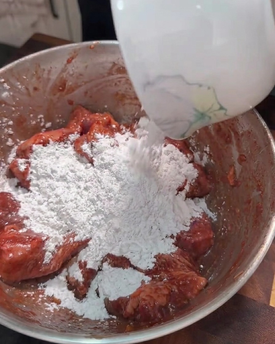 下味をつけた豚肉のボウルにサツマイモ澱粉を加えている様子