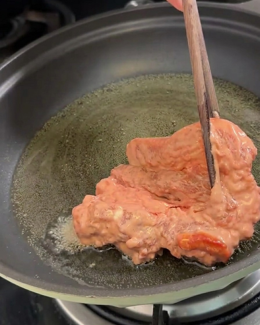 油の入った鍋に下味をつけて粉をまぶした豚肉を入れている様子