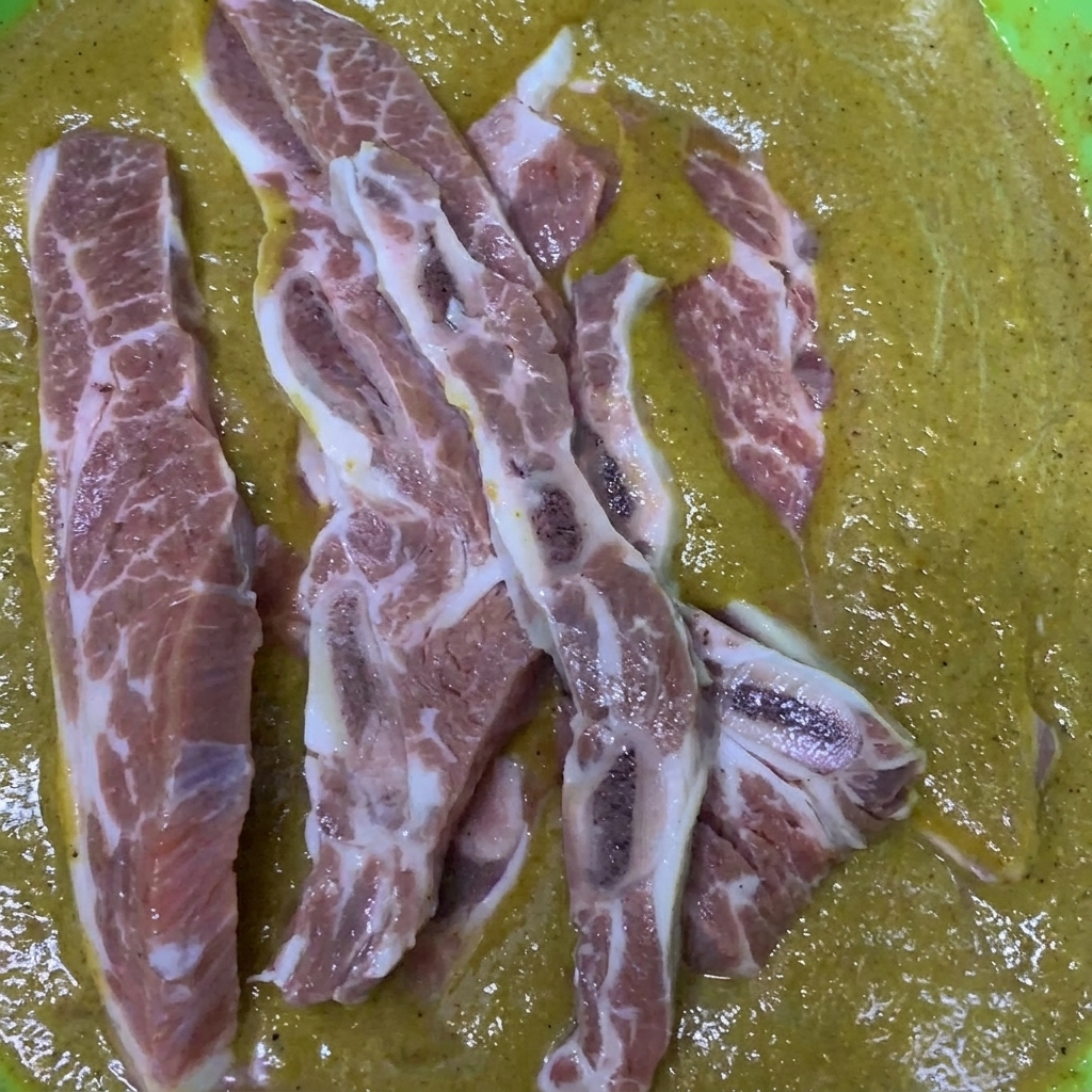 韓国風の特製ダレが入ったボウルで、骨付きカルビを混ぜ合わせて漬け込んでいる様子。