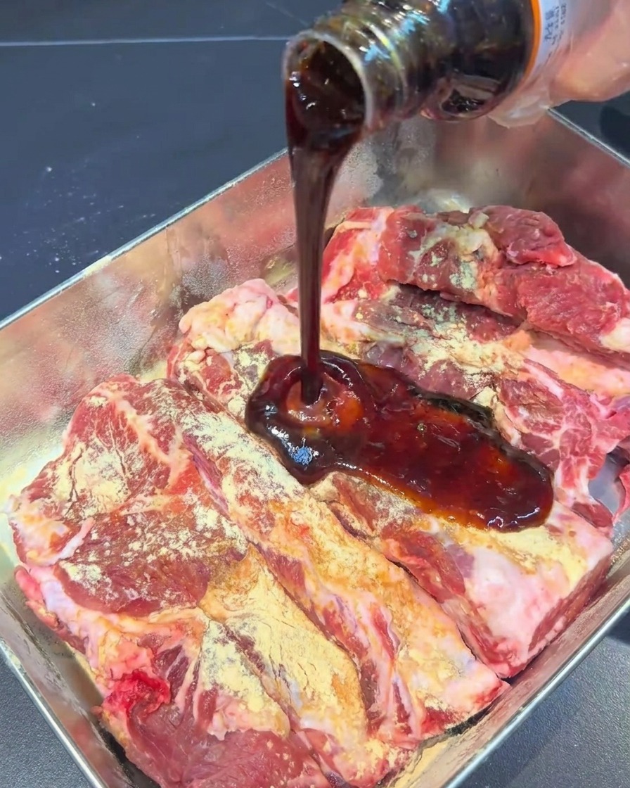 トレーの中のスペアリブに焼肉のタレを回しかけている様子。