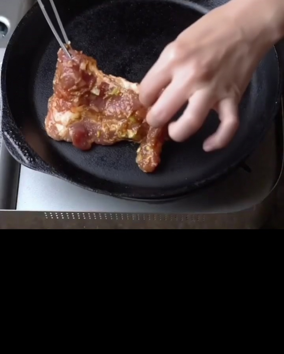 熱した鉄のフライパンで豚肉が焼けている様子。
