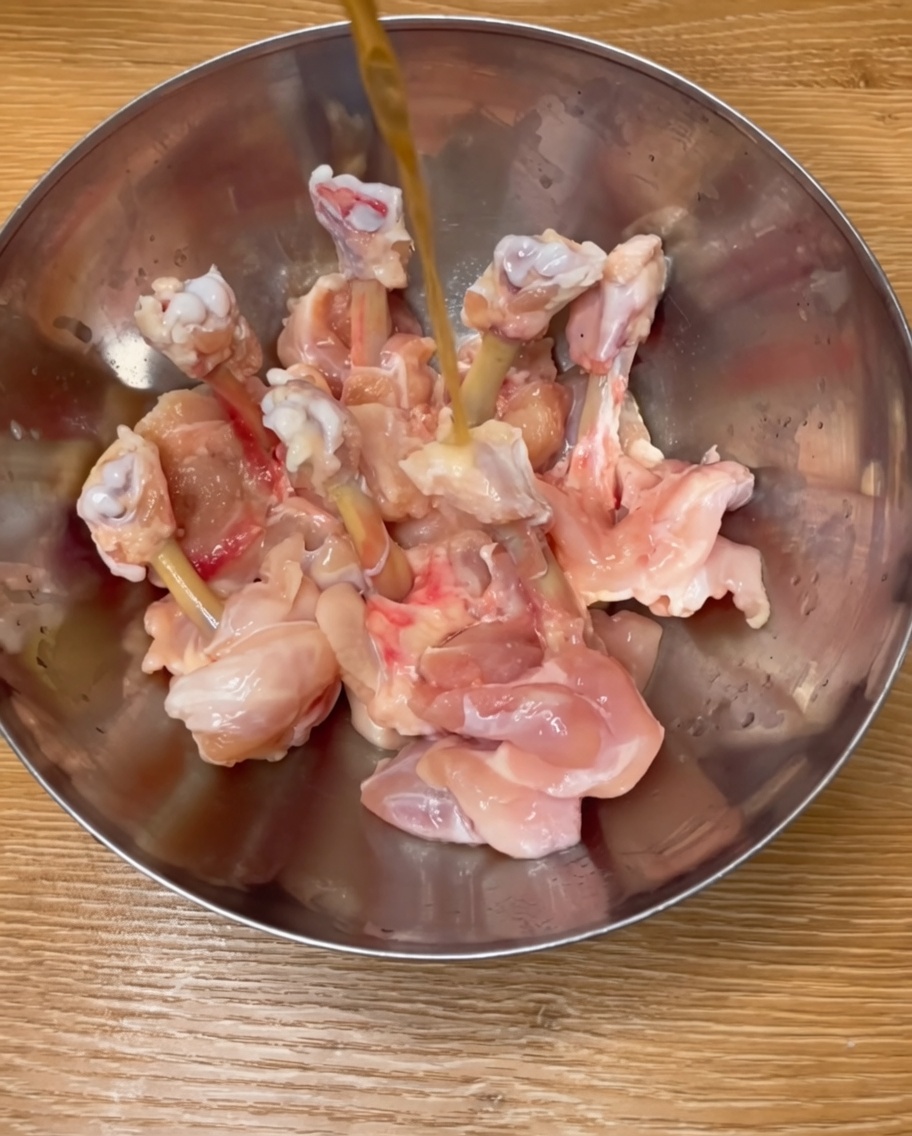金属製のボウルで、鶏ドラムスティックを料理酒、スパイス、溶き卵で和えている様子。