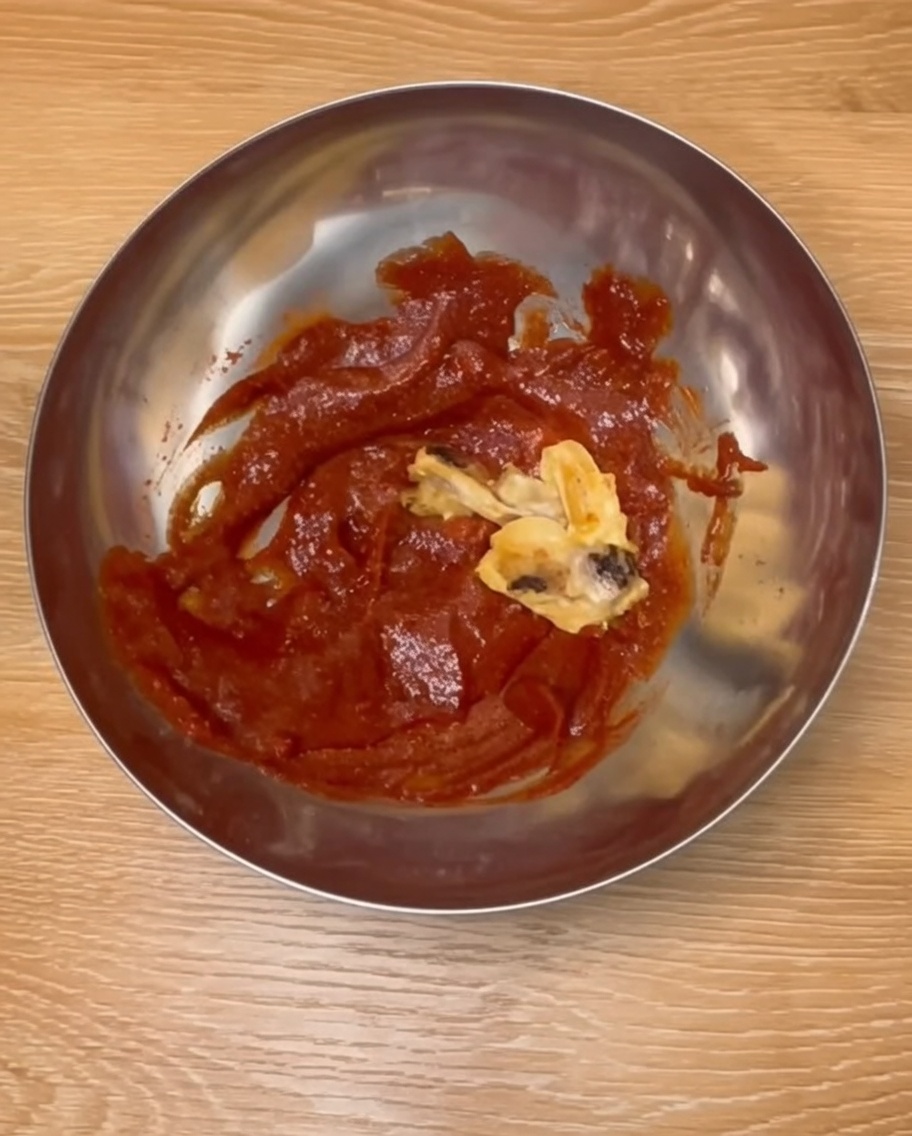 ステンレス製のボウルで、焼き上がった鶏ドラムスティックを赤い韓国風ソースと和えている様子。