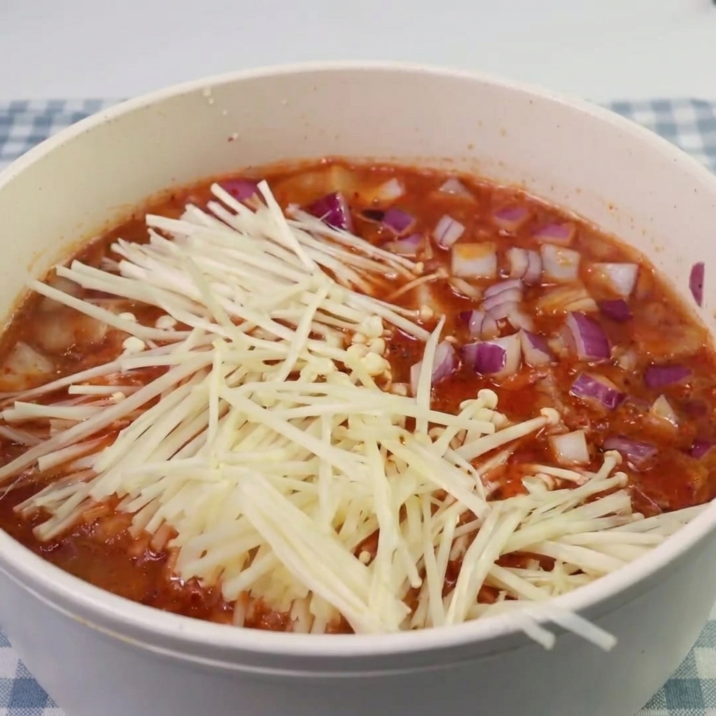 煮立ってきたキムチスープに、えのきとスパムを加えている様子。