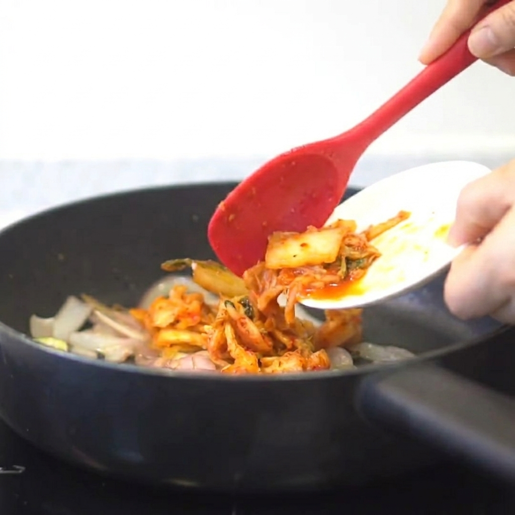 炒めた香味野菜にキムチが加えられている様子。
