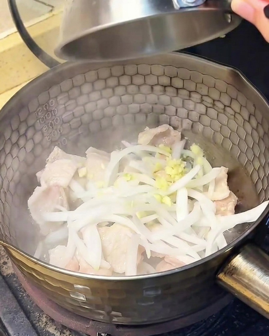 炒めた豚肉に玉ねぎとにんにくを加える様子。