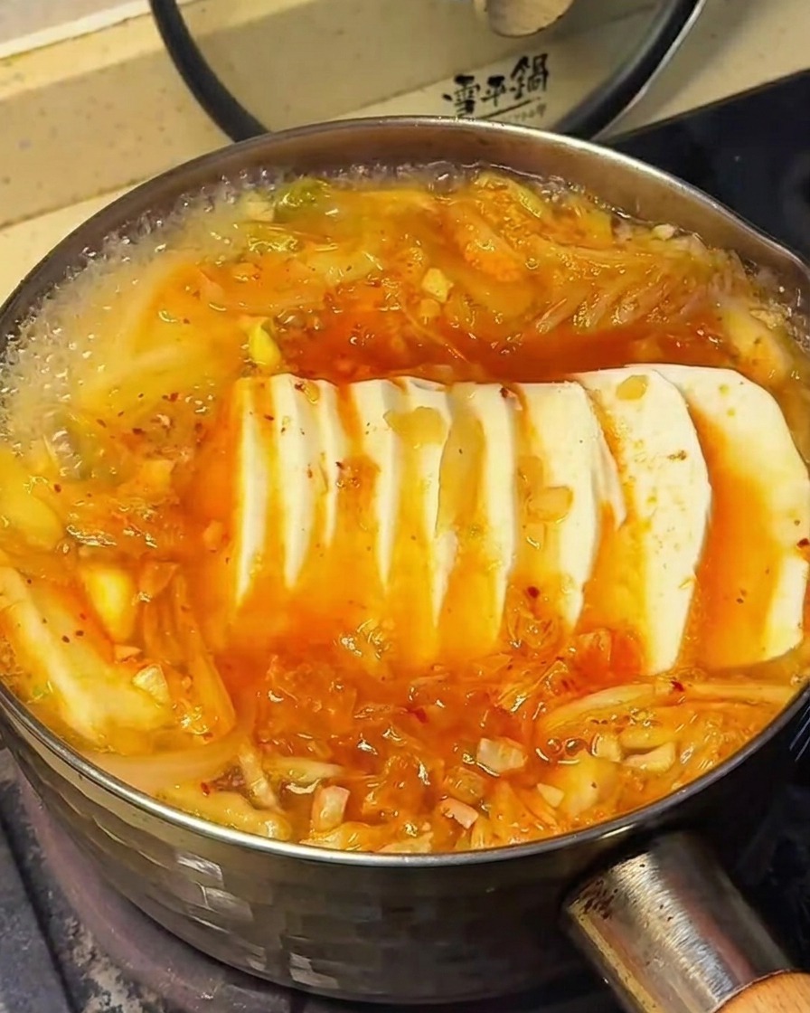 豆腐が入ったスープに調味料を振りかけている様子。