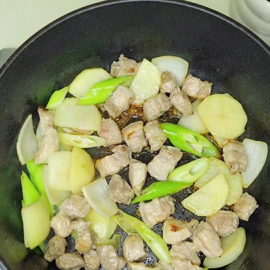 炒めた豚肉と玉ねぎにキムチを加えて混ぜている様子。