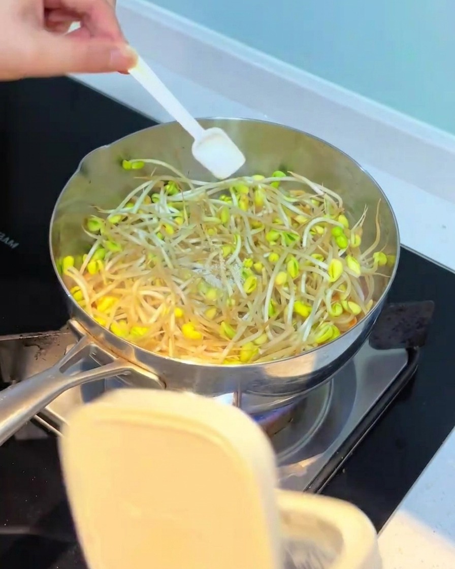 もやしが入った鍋に調味料を加えている様子。