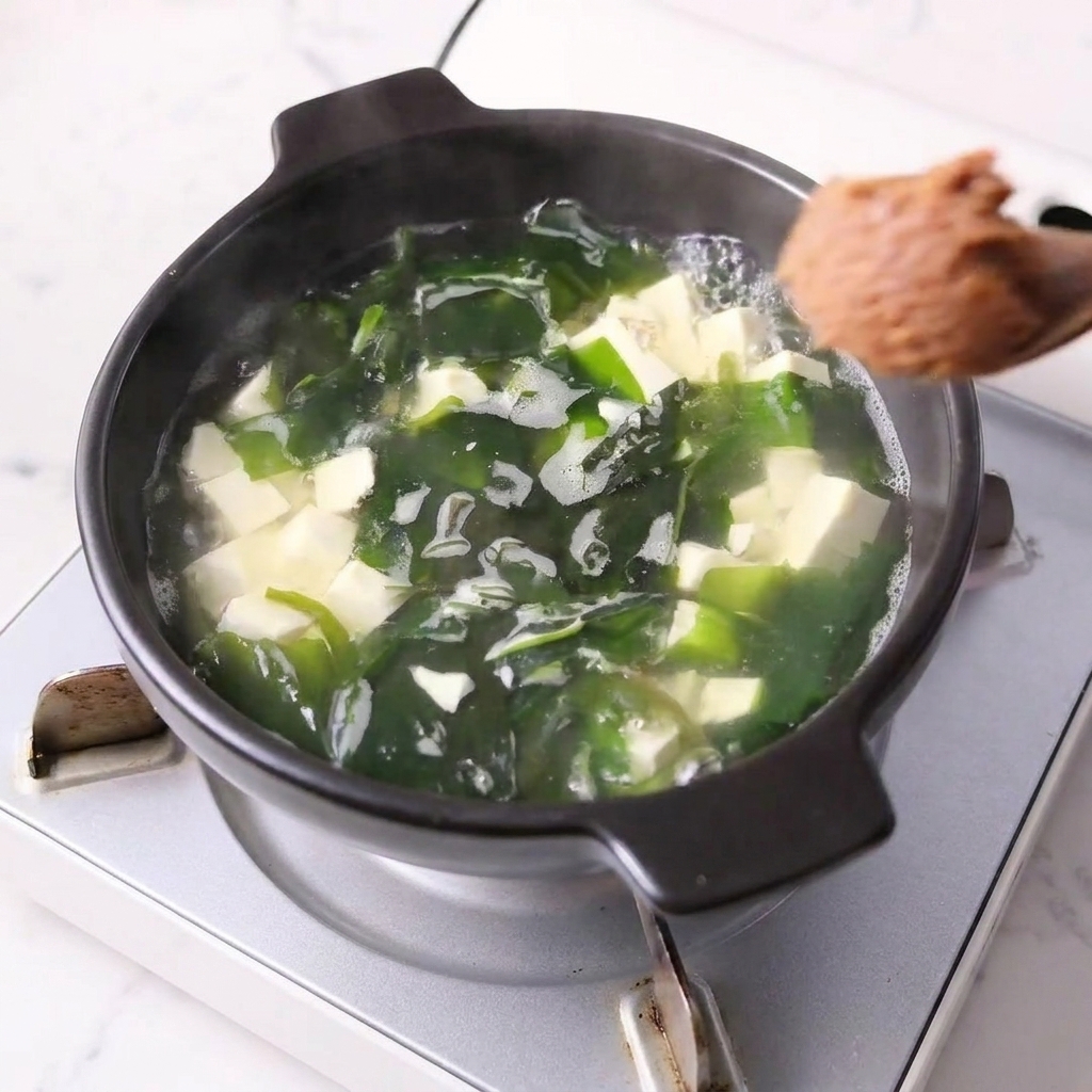 豆腐とわかめが入った鍋に味噌が溶かされている様子。