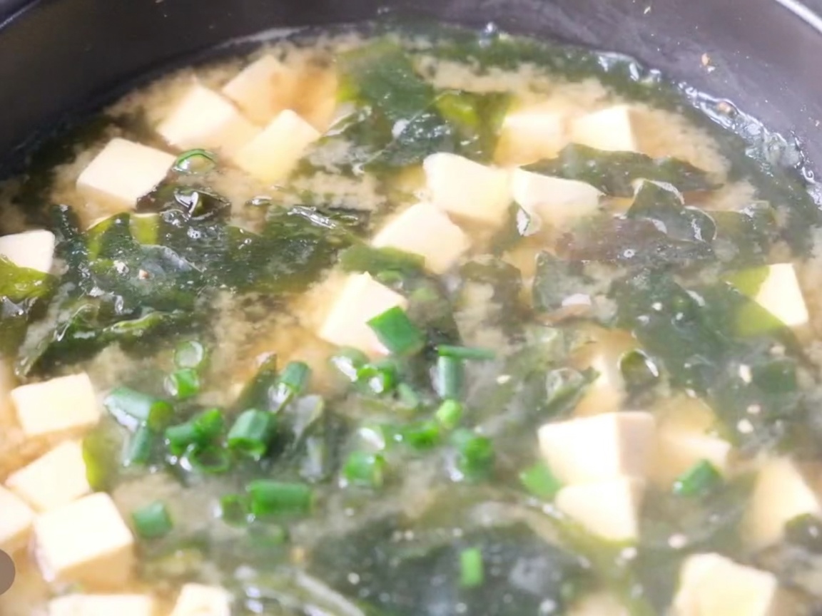 豆腐とわかめが入った出来立ての味噌汁に刻みネギがトッピングされた様子。
