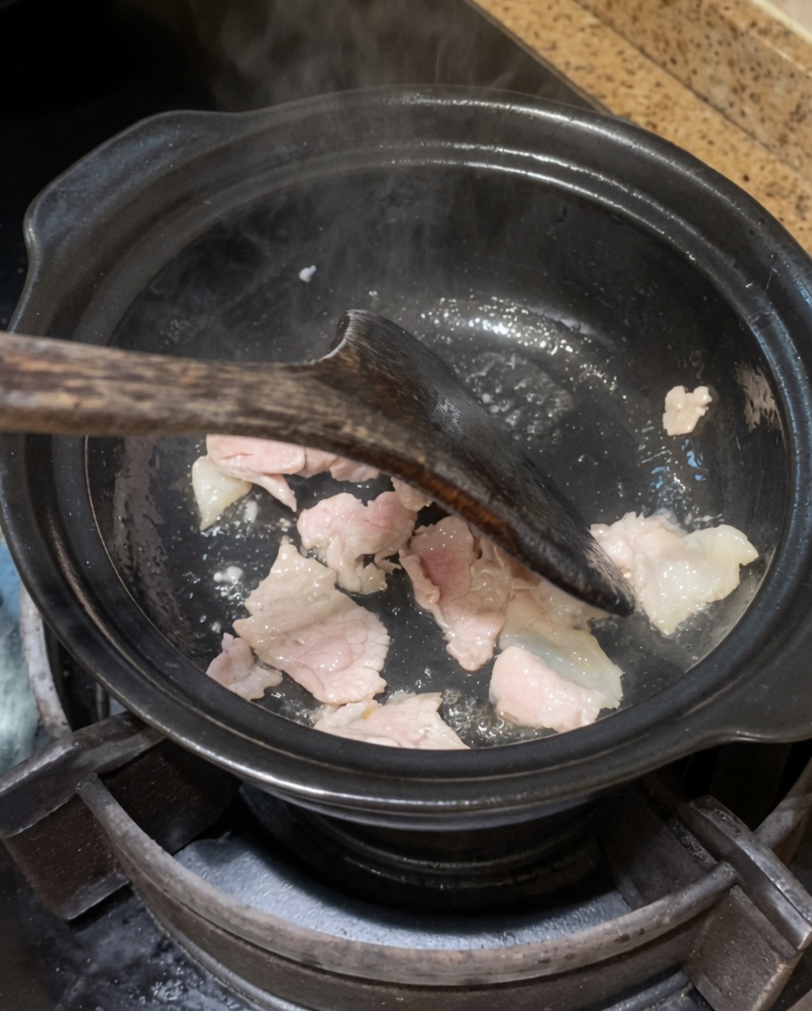 炒めた豚肉に玉ねぎとにんにくを加えて炒めている様子。