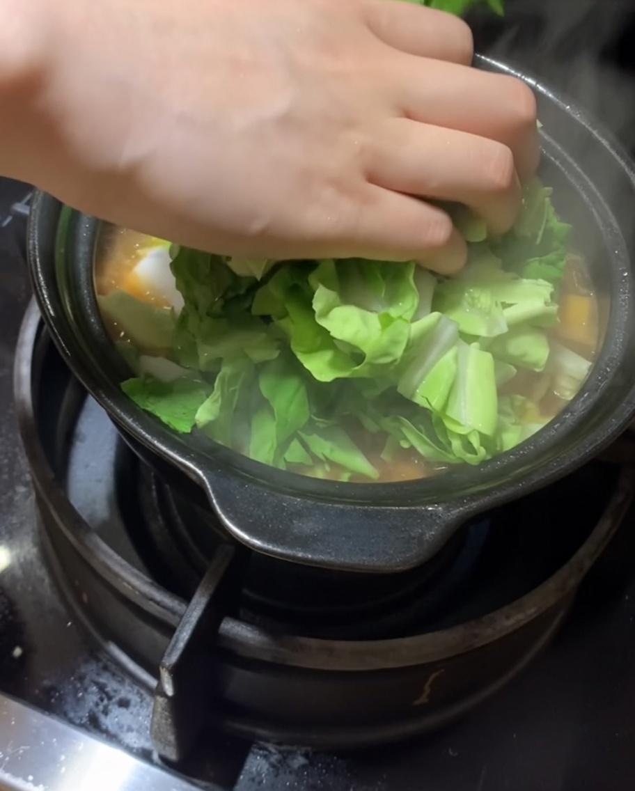 煮込み鍋に新鮮な葉物野菜を加えている様子。