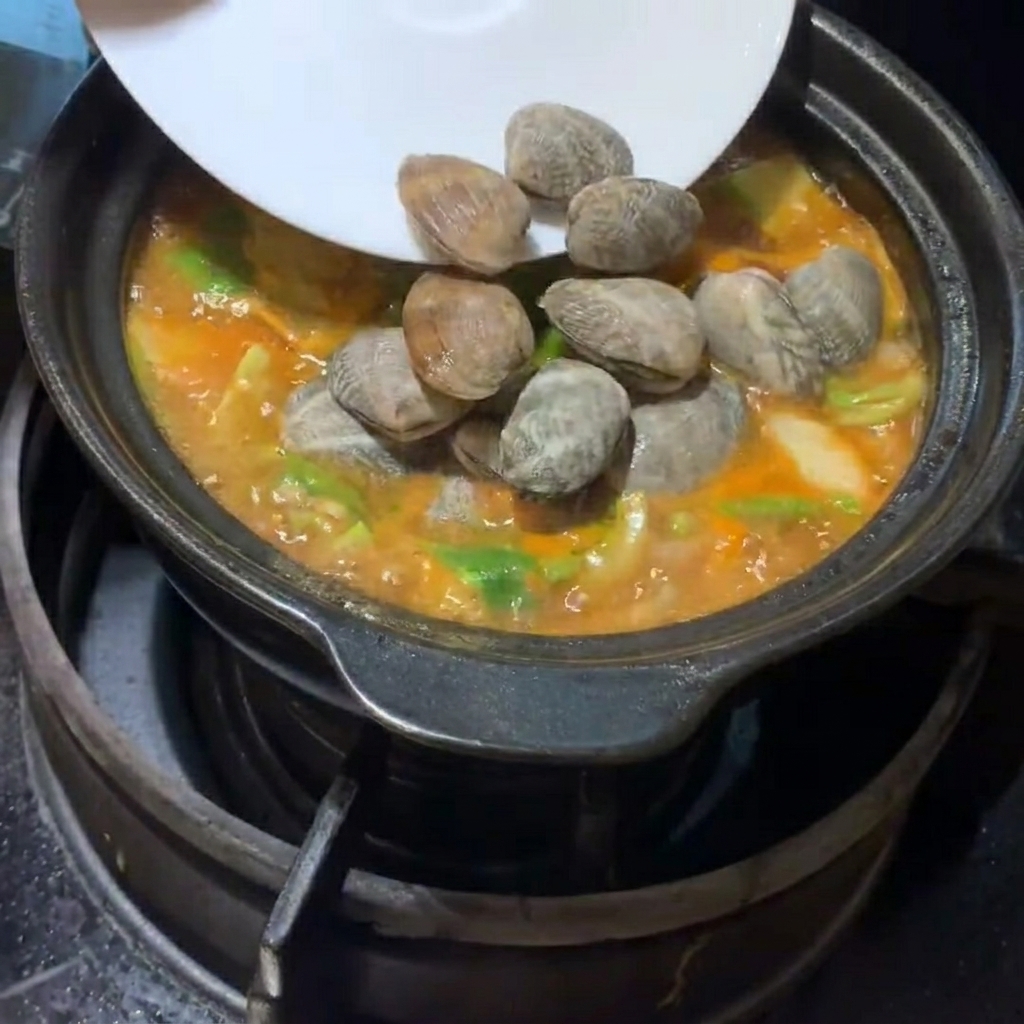 あさりと豆腐を鍋に静かに入れている様子。