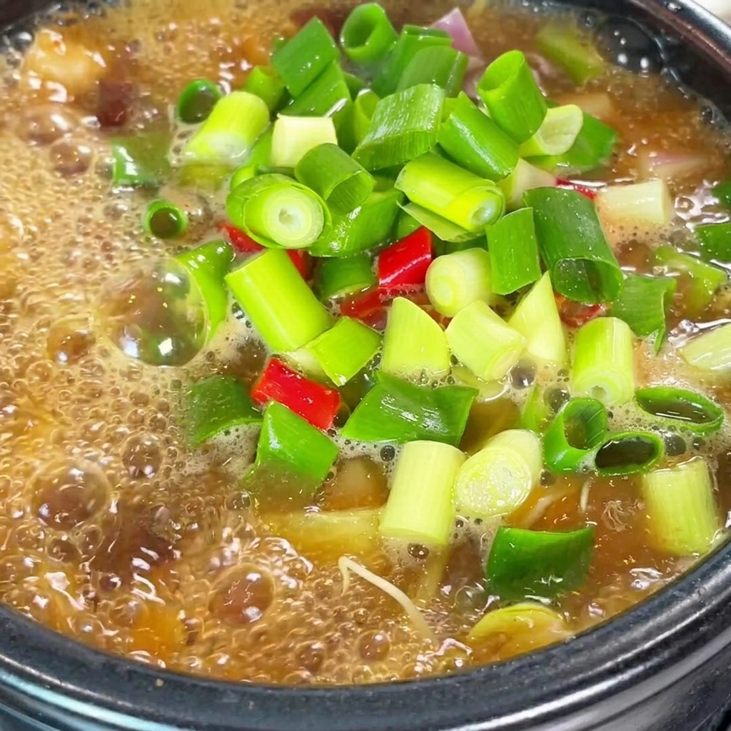 煮立っている鍋に粉唐辛子と牛肉だし粉末を入れている様子。