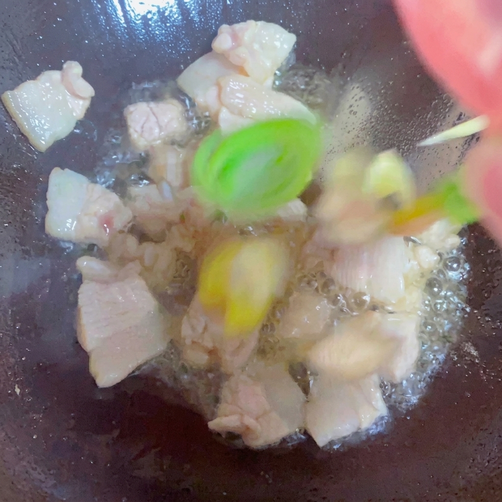 鍋で長ねぎ、生姜、にんにくを豚バラ肉と一緒に炒めている様子。