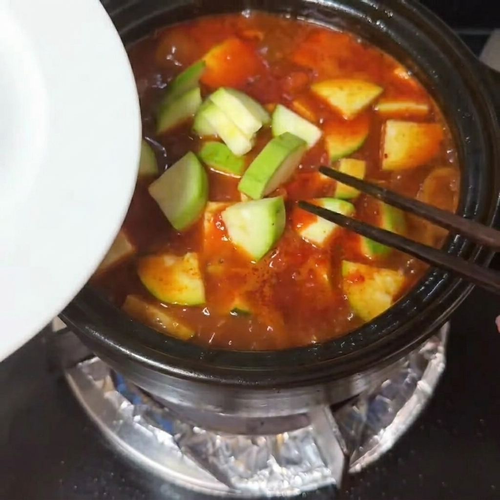 沸騰する赤いスープの中に、ズッキーニと柔らかな絹ごし豆腐が入れられている様子。